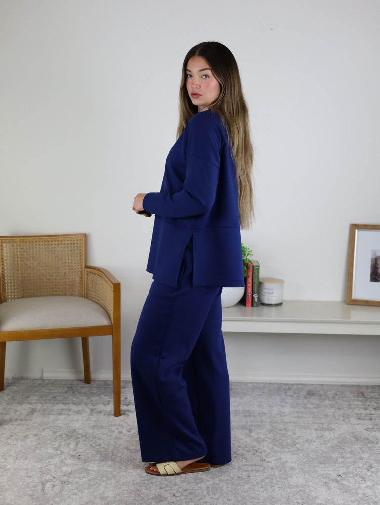 A woman wearing a dark blue Arbor Lounge Set with a long-sleeved pullover top featuring side slits and matching wide-leg trousers.
