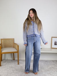 A woman with long hair wears the Bellamy Textured Striped Crochet Cardigan and wide-leg jeans, standing indoors beside a wooden chair and a white shelf with framed photos.
