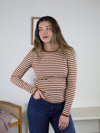 Mindy Ribbed Striped Top featuring a long-sleeved, ribbed knit design with terracotta and white horizontal stripes, worn with blue jeans.
