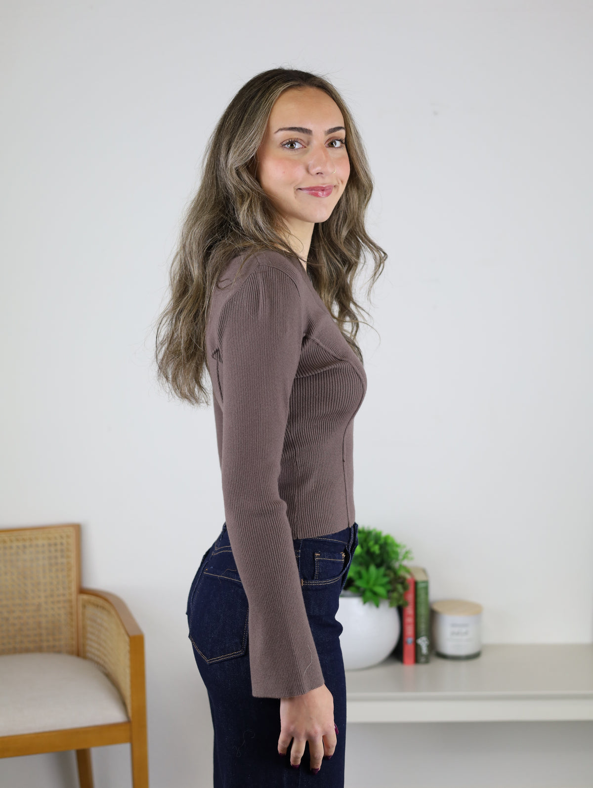 A person wearing a brown Luanne V-Neck Sweater in a fitted, ribbed style with dark blue jeans.