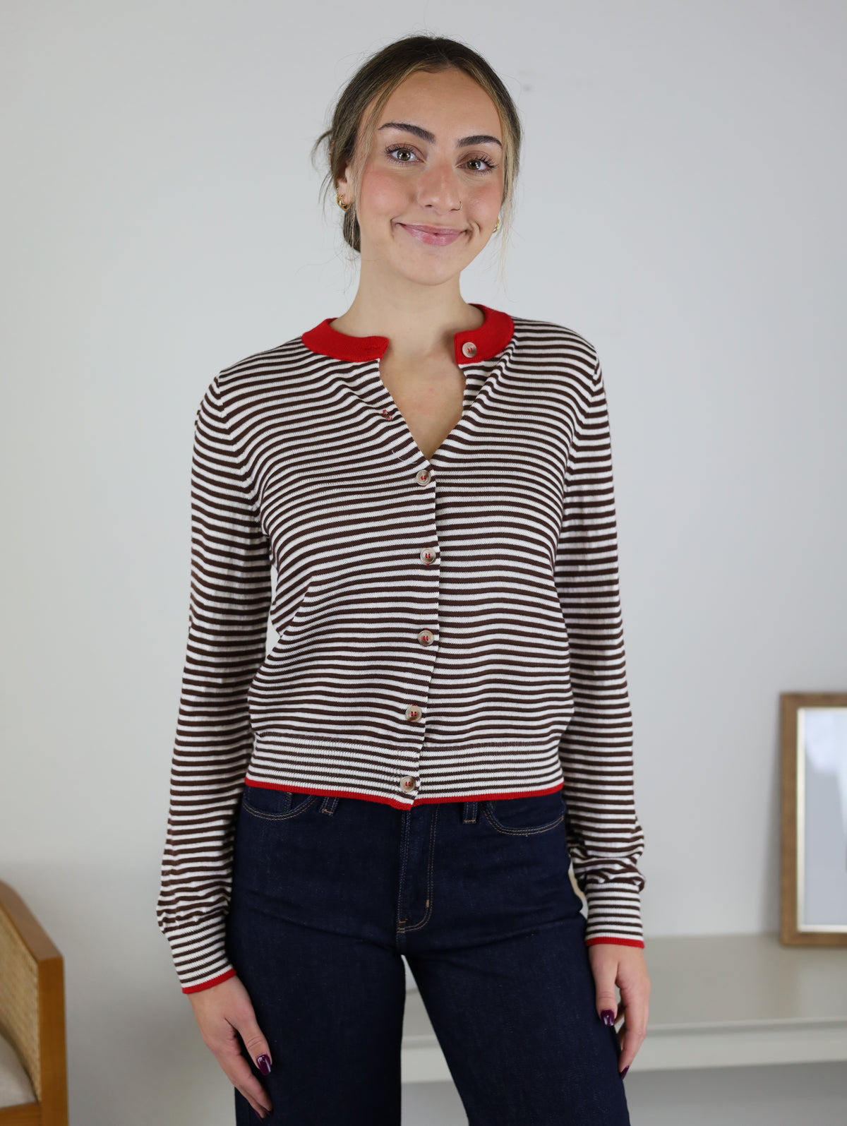 A person wears a Vera Striped Cardigan in brown and white with a contrasting red collar, cuffs, and hem, perfect for fall layering.