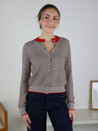 A person wears a Vera Striped Cardigan in brown and white with a contrasting red collar, cuffs, and hem, perfect for fall layering.