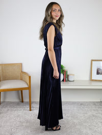 A woman wears the Petal Pleated Satin V Neck Maxi Dress, a sleeveless, navy blue empire waist maxi dress with a V-neckline and pleated detailing.