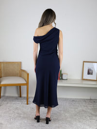 Back view of a person wearing the navy blue Abigail Asymmetrical Shoulder Midi Dress and black block-heeled sandals.