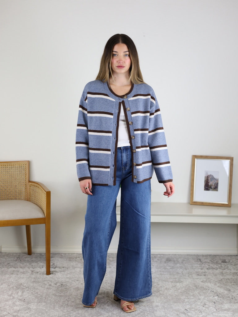 Woman wearing a blue, white, and brown Nora Stripe Button Down Knit Cardigan over a white top and blue wide-leg jeans.