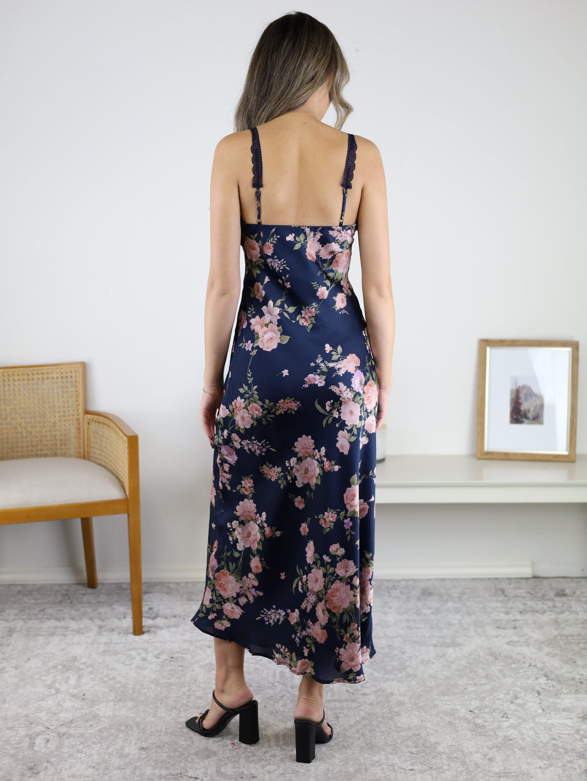 A woman seen from the back wearing a dark blue Kameron Floral Lace Trim Maxi Dress with lace-trimmed spaghetti straps and black block-heeled sandals.