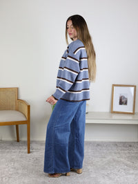 A woman wears the Nora Stripe Button Down Knit Cardigan, a light blue knit sweater with brown and white horizontal stripes, paired with wide-leg blue jeans.