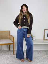 A woman wears a brown Maya Contrast Hem Cardigan with a boxy fit and light green trim at the neckline, cuffs, and hem, paired with wide-leg blue jeans.