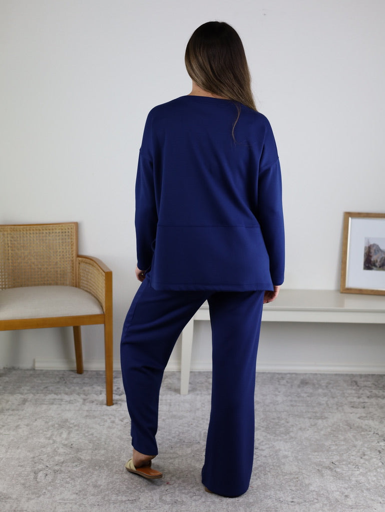 A person wearing a navy blue Arbor Lounge Set stands facing away from the camera.