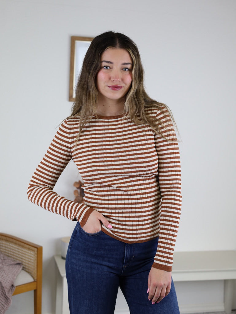A person wearing a terracotta stripe Mindy Ribbed Striped Top with long sleeves and dark blue jeans.