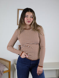 A person wearing a terracotta stripe Mindy Ribbed Striped Top with long sleeves and dark blue jeans.