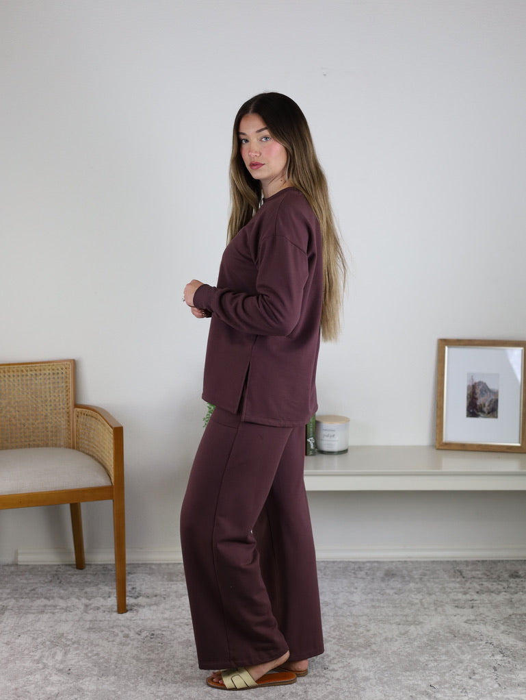 A person wearing a matching dark plum-colored long-sleeve top with side slits and Adaline Wide Leg Sweatpants.