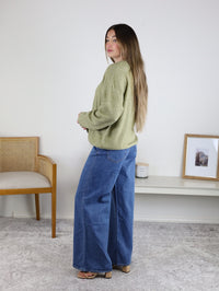 A person wearing an Olive Oversized Cardigan and wide-leg blue jeans.