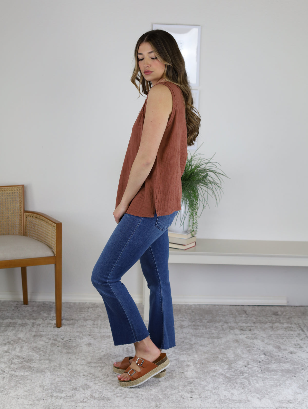 A person wearing a rust-colored sleeveless top and High Rise Tonal Crop Flare Denim with raw hems, paired with brown platform sandals.