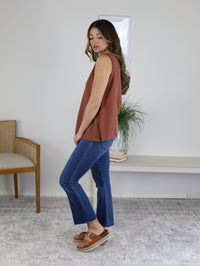 A person wearing a rust-colored sleeveless top and High Rise Tonal Crop Flare Denim with raw hems, paired with brown platform sandals.