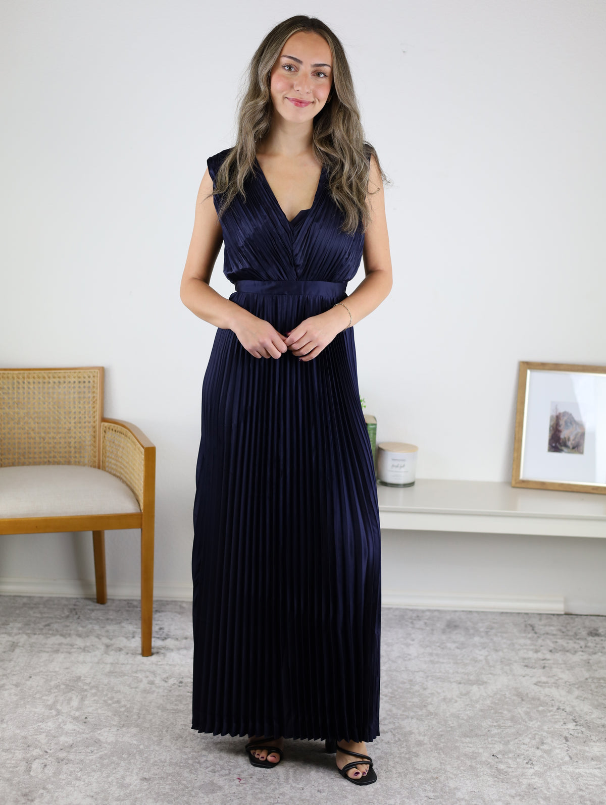 A woman wearing a navy blue Petal Pleated Satin V Neck Maxi Dress with a sleeveless, pleated design and a V-neckline.