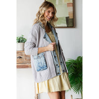 A smiling woman with wavy blonde hair wears the Veveret - Knit Body Denim Layerd Jacket: Cream / Denim / L over a loose yellow dress, standing indoors by a wooden table, green plant, and framed wall art.