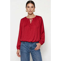 Naked Zebra - Long Sleeve Draped Bubble Hem Blouse in wine, featuring a long-sleeved satin design with a gathered, draped bubble hem and a tie-neck detail, worn with blue jeans.