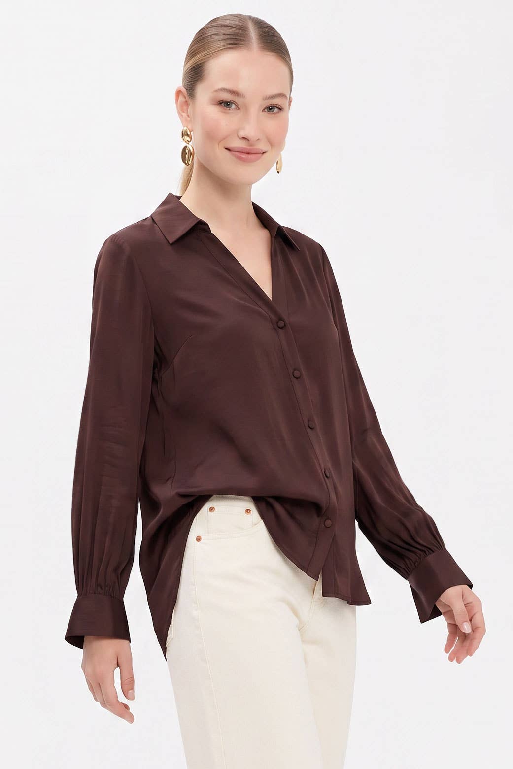 A woman wears a Naked Zebra - Neck Shirt With Open Seam Sleeve: Black / L in dark brown woven polyester with open seam sleeves, paired with white jeans.