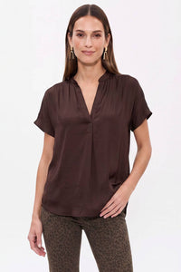 A woman wearing a Naked Zebra - Drop Shoulder Regular Blouse: Chocolate / L, a chocolate brown, short-sleeved drop shoulder blouse with a V-neckline.