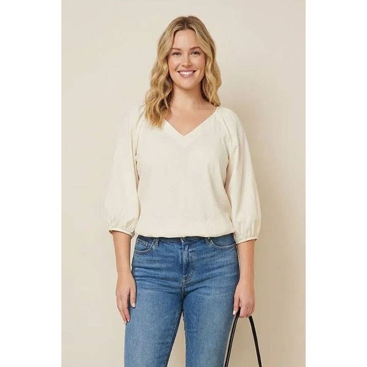 A smiling woman wearing a Naked Zebra - Elastic Puff Sleeve V-neck Blouse: Burgundy / L, styled with puff sleeves and blue jeans.