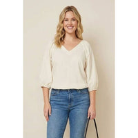 A smiling woman wearing a Naked Zebra - Elastic Puff Sleeve V-neck Blouse: Burgundy / L, styled with puff sleeves and blue jeans.