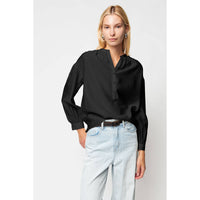 An elegant Naked Zebra - Button-down Blouse With Gathered Neckline: Black / L, featuring a gathered neckline and cuffed sleeves, worn tucked into light-wash jeans.