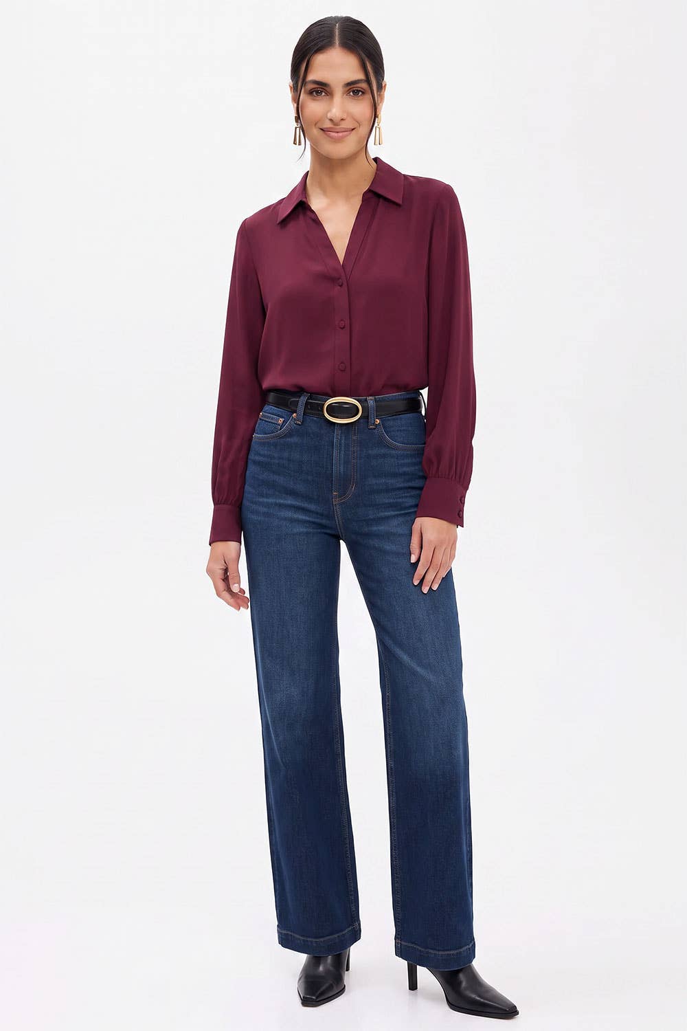 A woman wearing a Naked Zebra - Neck Shirt With Open Seam Sleeve: Wine / L tucked into dark wash high-waisted jeans with a black belt.