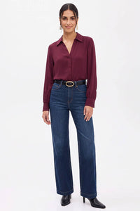 A woman wearing a Naked Zebra - Neck Shirt With Open Seam Sleeve: Wine / L tucked into dark wash high-waisted jeans with a black belt.