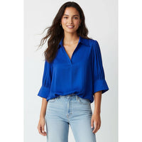 A woman wearing a bright blue Naked Zebra - Half Sleeve Hi-lo Bubble Hem Blouse: Wine / L with half-length sleeves and light-wash blue jeans.