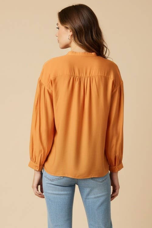 Back view of a woman wearing an elegant, long-sleeved, mustard-colored Naked Zebra - Button-down Blouse With Gathered Neckline with a gathered neckline and blue jeans.