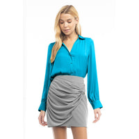 A woman wearing a Naked Zebra - Neck Shirt With Open Seam Sleeve: Black / L tucked into a gray mini skirt with a gathered, draped front.