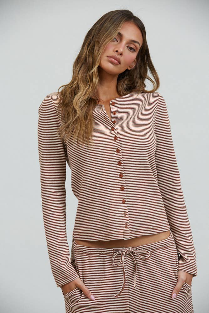 A woman with long wavy hair is wearing the Creamon CTP3592 Lounge Striped Button Down Top & Pants Set in brown stripe, which features a coordinating button-down top and wide-leg pants, while standing against a plain light background.