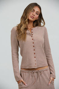 A woman with long wavy hair is wearing the Creamon CTP3592 Lounge Striped Button Down Top & Pants Set in brown stripe, which features a coordinating button-down top and wide-leg pants, while standing against a plain light background.