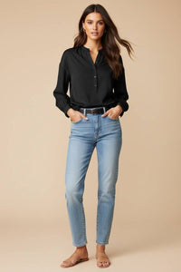 A woman wearing a Naked Zebra - Button-down Blouse With Gathered Neckline in black, featuring long sleeves, tucked into light-wash blue jeans with a black belt.