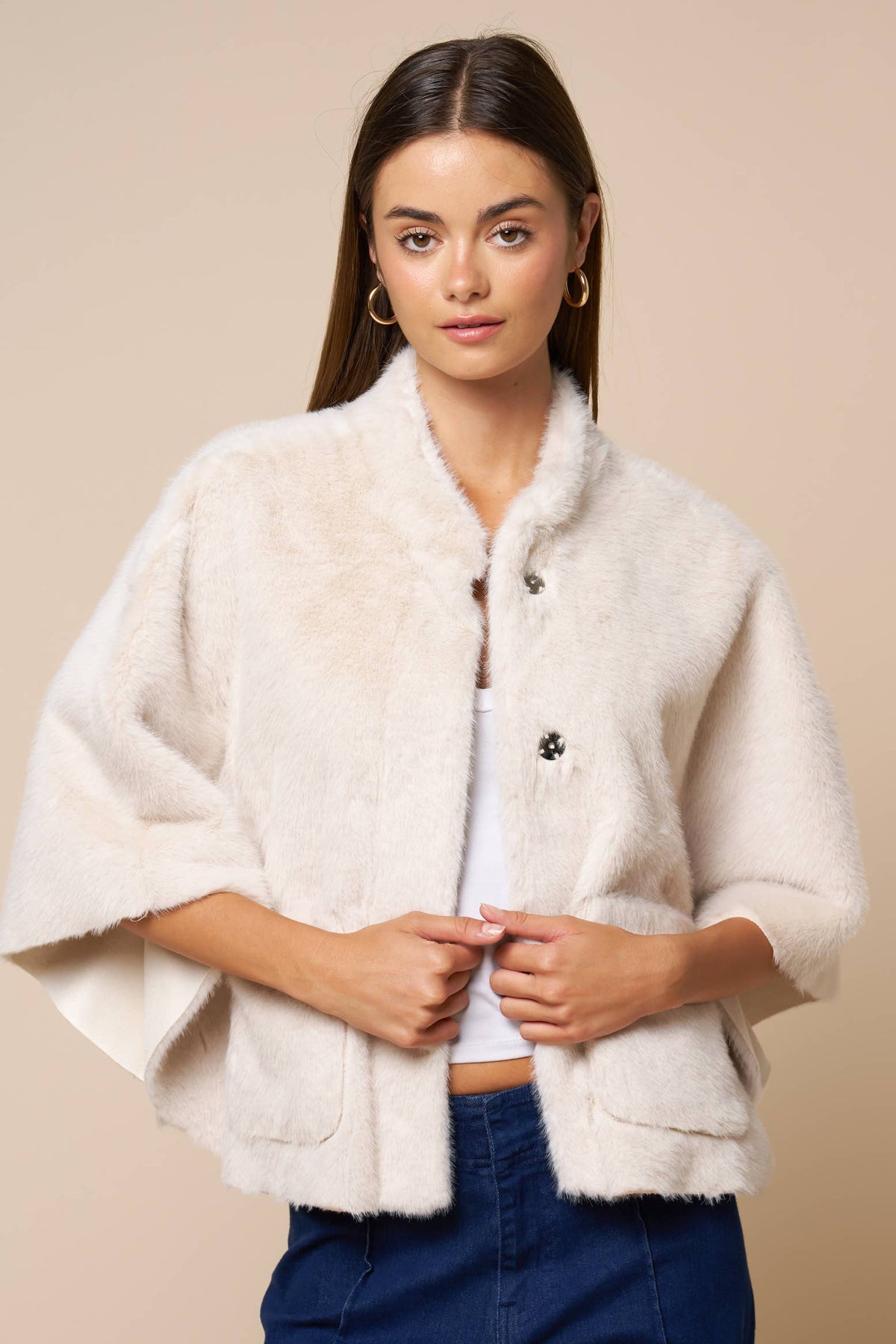 A person wears a cream-colored Jordan Fur Cape Sleeve Jacket with wide sleeves and button closures.