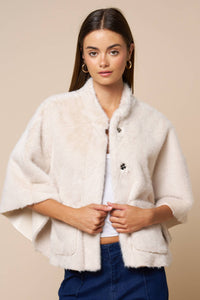 A person wears a cream-colored Jordan Fur Cape Sleeve Jacket with wide sleeves and button closures.