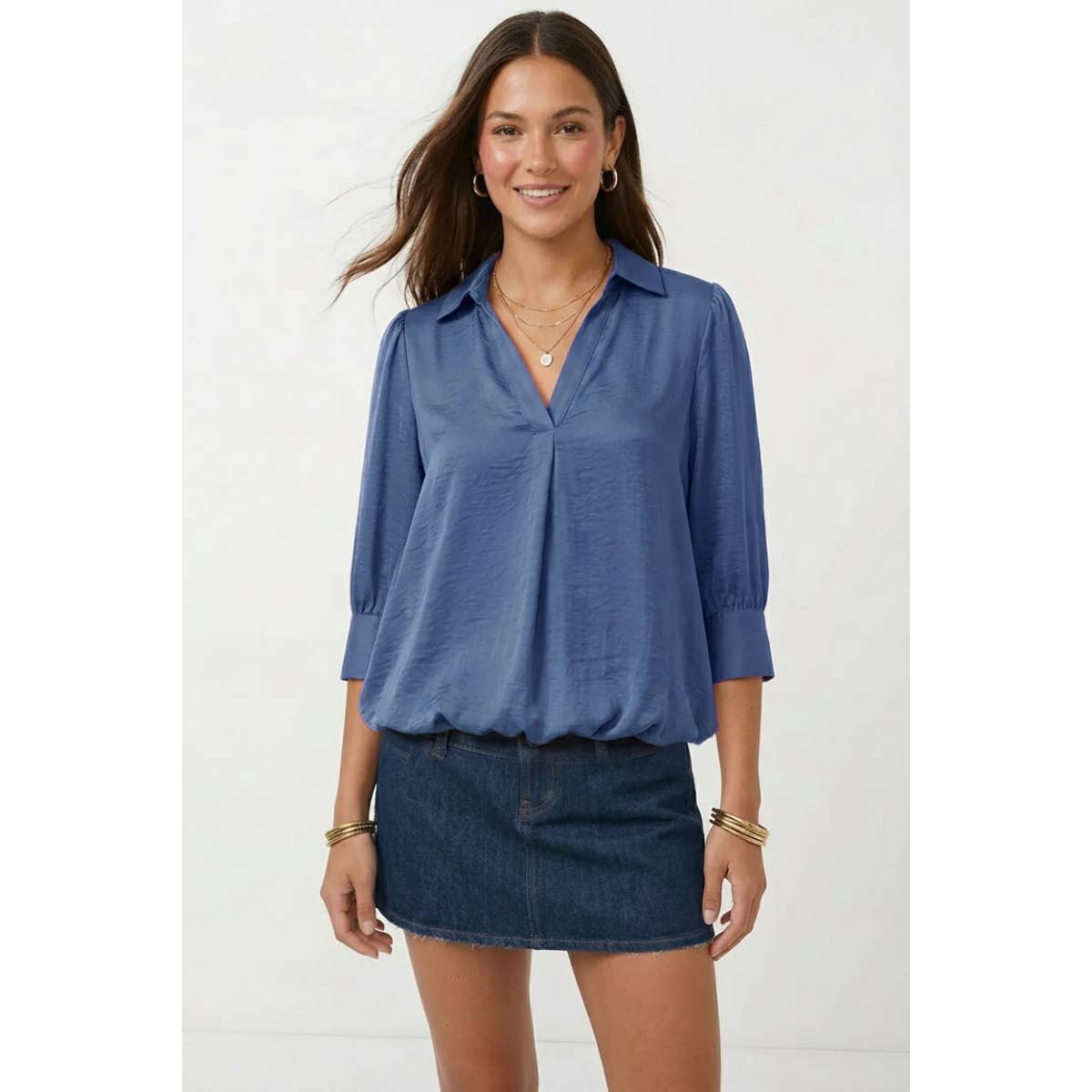 A woman wears a Naked Zebra - Half Sleeve Hi-lo Bubble Hem Blouse in blue with half-sleeves and a bubble hem, paired with a dark denim mini skirt.