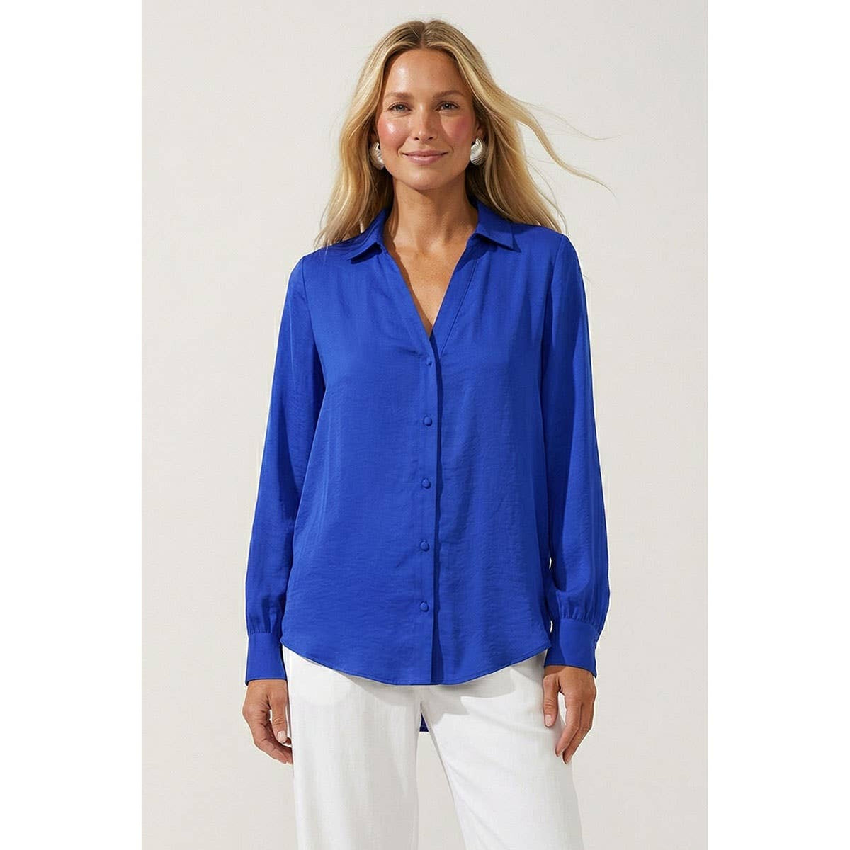 A woman wears a royal blue, woven polyester Naked Zebra - Neck Shirt With Open Seam Sleeve: Wine / L featuring a collared V-neck and white trousers.