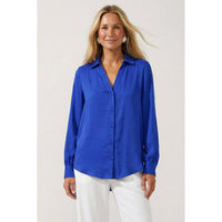 A woman wears a royal blue, woven polyester Naked Zebra - Neck Shirt With Open Seam Sleeve: Wine / L featuring a collared V-neck and white trousers.