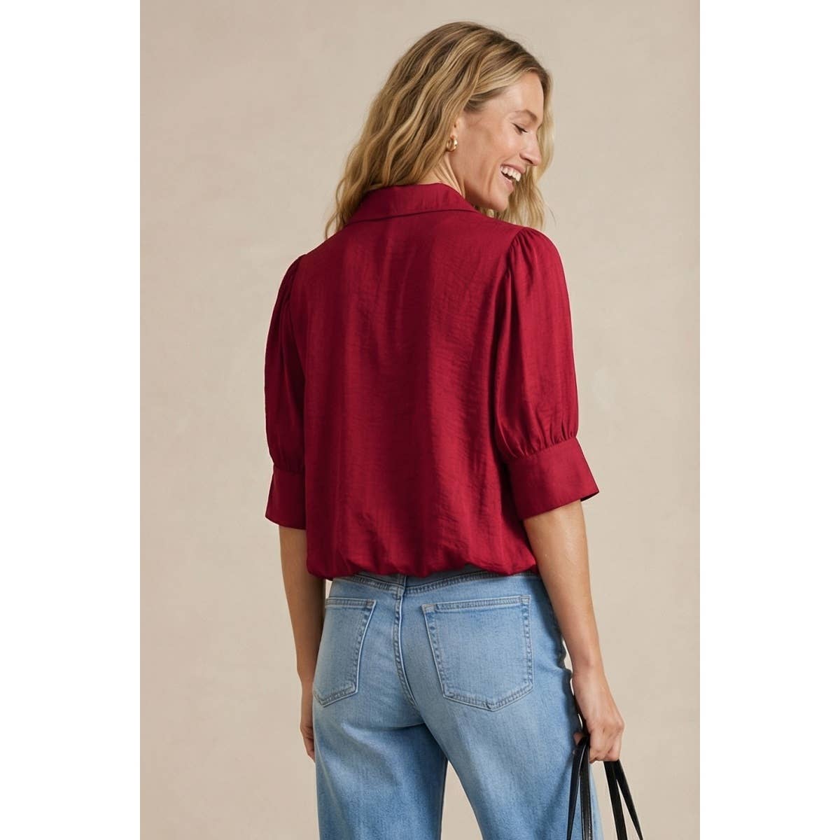 A woman wears a wine-colored Naked Zebra - Half Sleeve Hi-lo Bubble Hem Blouse, featuring a collared neckline and half sleeves, paired with light-wash jeans.