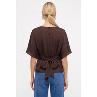 A dark navy Naked Zebra - Back Tie Dolman Sleeve Silky Fall Blouse with a tie-back waist, worn with blue jeans.
