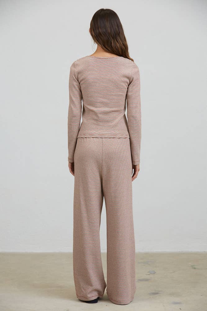 Wearing the Creamon - CTP3592 BROWN Lounge Striped Button Down Top & Pants Set in Brown Stripe, a person with long brown hair stands facing a plain white wall with their back to the camera.