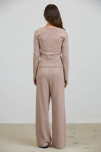Wearing the Creamon - CTP3592 BROWN Lounge Striped Button Down Top & Pants Set in Brown Stripe, a person with long brown hair stands facing a plain white wall with their back to the camera.