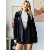 A woman stands indoors wearing the Veveret - Knit Body Denim Layerd Jacket: Cream / Denim / L over a white ribbed crop top and black shorts, with abstract art and a green console table in the background.