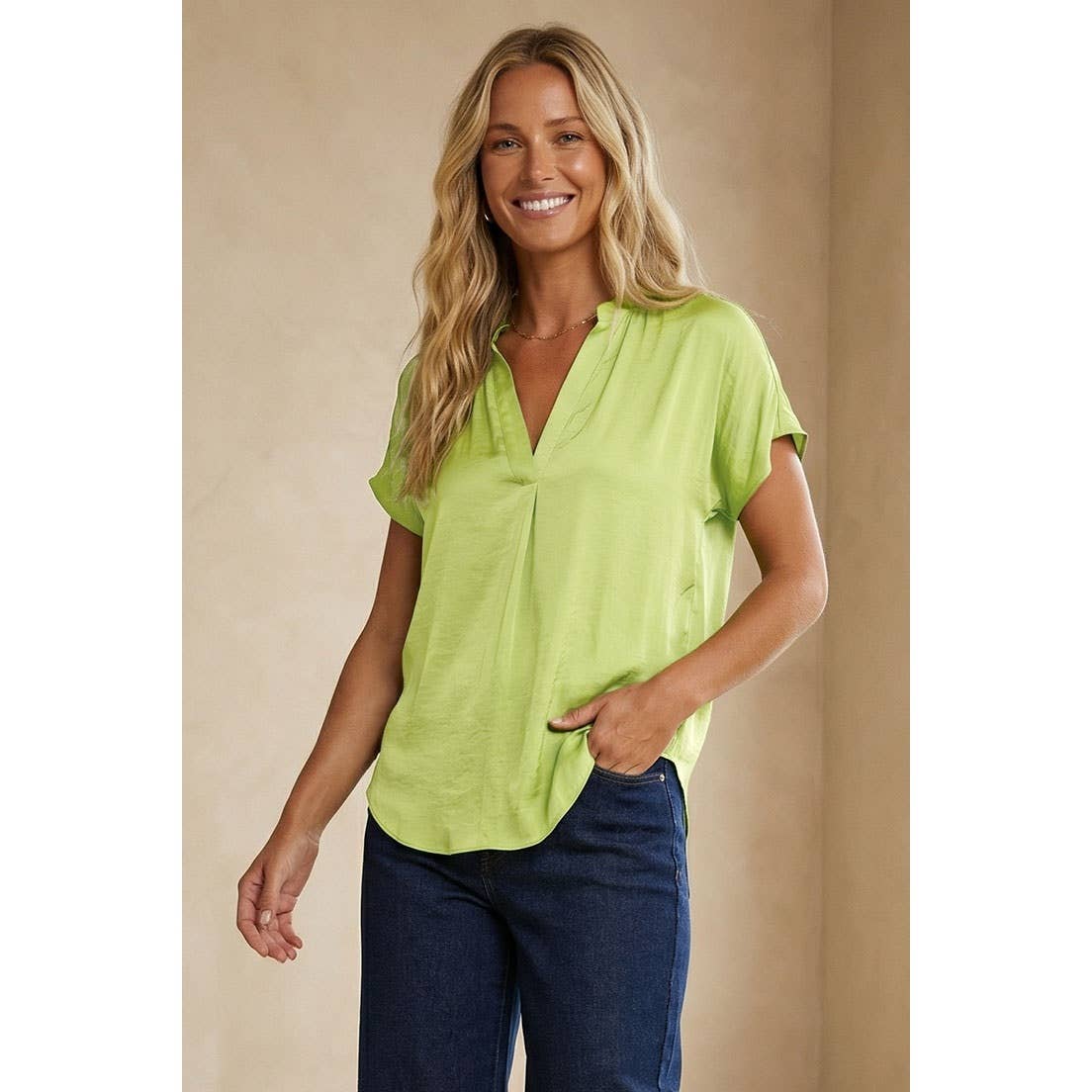 A smiling woman wearing a lime green Naked Zebra - Drop Shoulder Regular Blouse: Chocolate / L with a notched neckline and dark blue jeans.