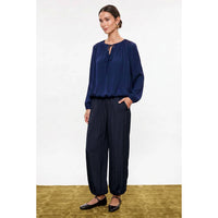 A model wears a Naked Zebra - Long Sleeve Draped Bubble Hem Blouse: Wine / L in navy blue with a bubble hem and matching cuffed trousers.