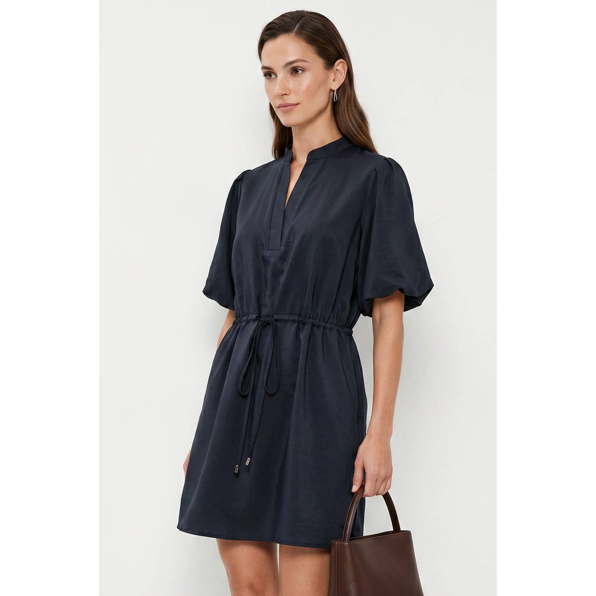 A woman wears a Naked Zebra - Puff Sleeve Cinched Waist Mini Dress: Navy / L, featuring a navy puff sleeve mini dress with a mandarin collar and a drawstring cinched waist, while holding a brown handbag.