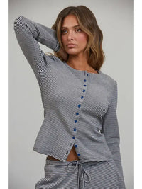 A woman in the Creamon - CTP3592 BROWN Lounge Striped Button Down Top & Pants Set, featuring brown stripes, an asymmetrical button-down top, and matching wide leg pants, stands with one hand behind her head, gazing off to the side.