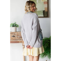 Woman with blonde wavy hair, wearing the Veveret - Knit Body Denim Layerd Jacket: Cream / Denim / L, stands indoors with her back to the camera; a plant, wooden table, and framed art are visible behind her.